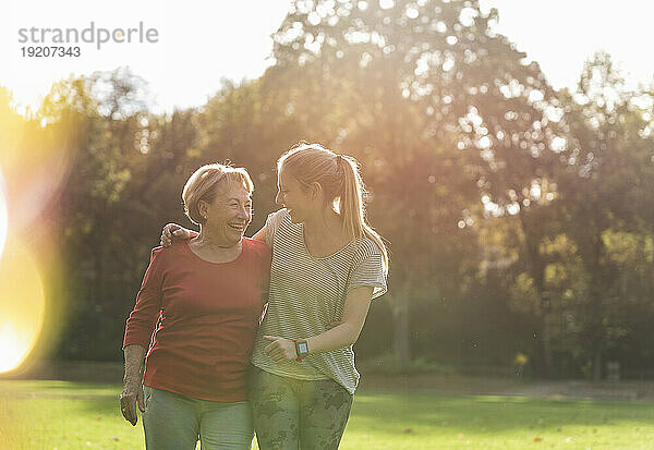 Fitte Großmutter und Enkelin gehen mit Armen im Park spazieren
