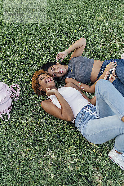 Zwei glückliche Freundinnen entspannen sich in einem Park und hören Musik