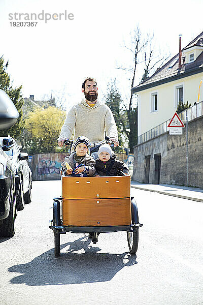 Glücklicher Vater mit zwei Kindern  die mit dem Lastenrad durch die Stadt fahren