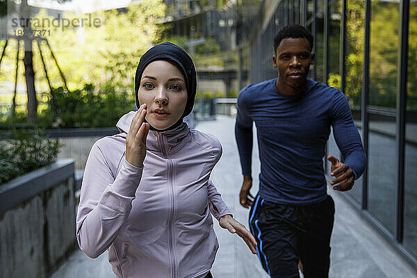 Entschlossene Frau im Hijab rennt mit Freundin auf Fußweg