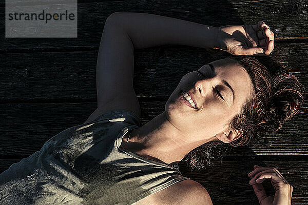 Portait of a happy woman lying on a jetty in sunlight