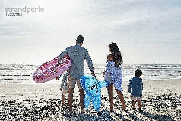 Familie mit aufblasbarem Schwimmring und Spielzeughai steht zusammen am Strand
