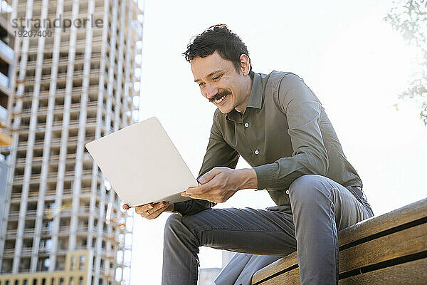 Lächelnder Geschäftsmann mit Laptop sitzt im Büropark