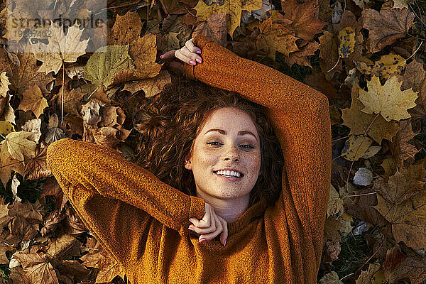 Lächelnde rothaarige Frau liegt auf Herbstblättern im Park