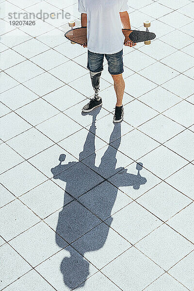Junger Mann mit Beinprothese hält Skateboard