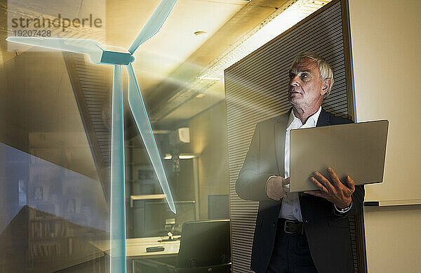 Digitales zusammengesetztes Bild eines Geschäftsmannes  der im Büro eine futuristische Windkraftanlage betrachtet