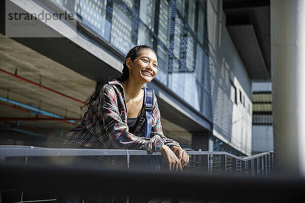 Lächelnder Student steht neben dem Geländer der Universität