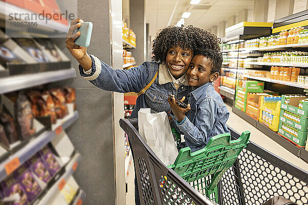 Glückliche Frau macht Selfie mit ihrem Sohn  der im Einkaufswagen sitzt