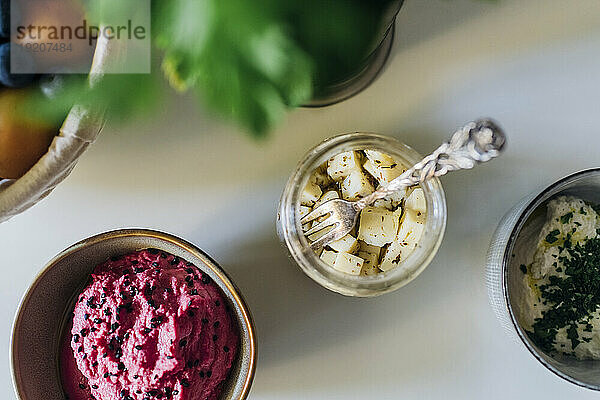 Beetroot hummus with jar of pickle on table