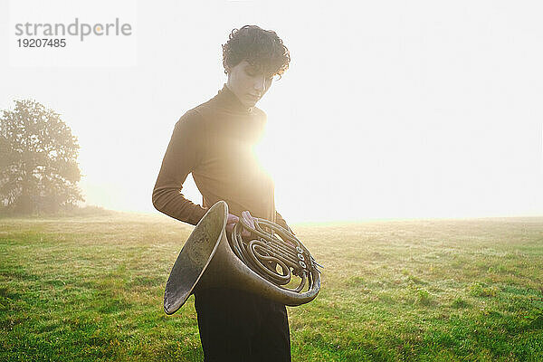 Musician holding trumpet in meadow at sunrise