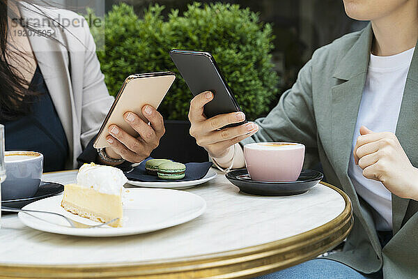 Geschäftspartner nutzen Smartphones mit Kaffee und Kuchen auf dem Tisch im Straßencafé