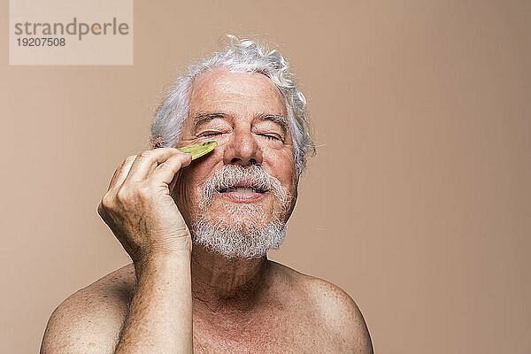 Senior man with eyes closed massaging face with Gua Sha