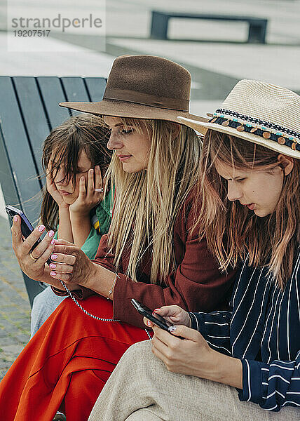 Mutter und Tochter benutzen Mobiltelefon auf Bank