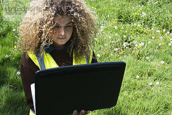 Geschäftsfrau mit lockigem Haar benutzt Laptop im Gras