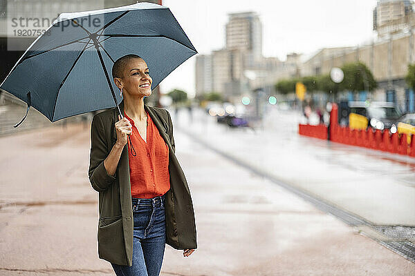 Lächelnde Frau mit Regenschirm steht auf Fußweg