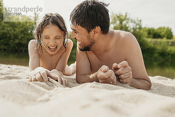 Fröhlicher Vater und Sohn liegen im Sand und genießen den Strand