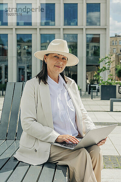 Lächelnde Geschäftsfrau sitzt mit Laptop auf der Bank