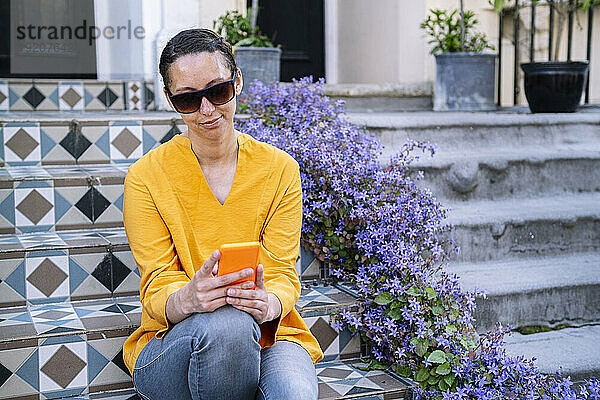 Frau mit Sonnenbrille und Smartphone sitzt auf Stufen