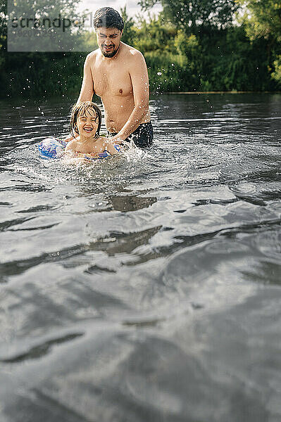 Glücklicher Mann bringt seinem Sohn im Fluss Schwimmen bei