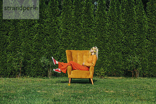 Blonde Frau sitzt auf einem Sessel im Garten