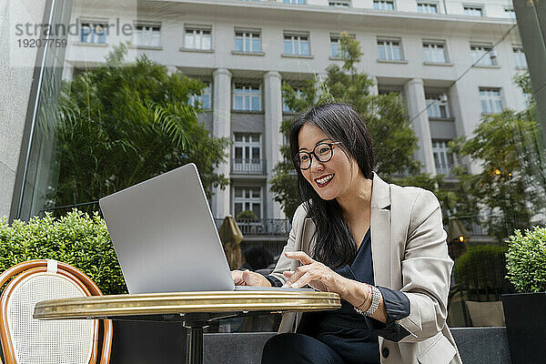 Lächelnde Geschäftsfrau  die im Straßencafé am Laptop arbeitet