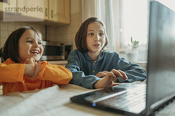 Glückliche Brüder schauen sich Online-Unterricht am Esstisch an