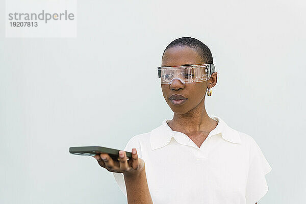 Junge Frau mit Smart-Brille steht mit Smartphone