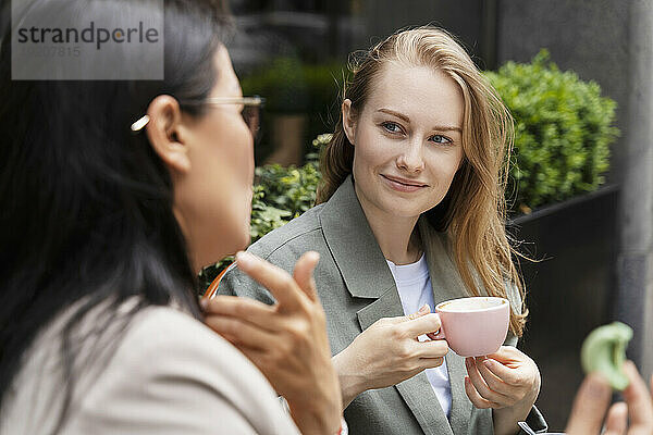 Geschäftsfrau hält Kaffeetasse in der Hand und diskutiert mit Partner im Straßencafé