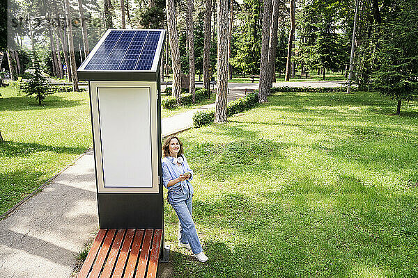 Frau lehnt an Solarladestation im Park