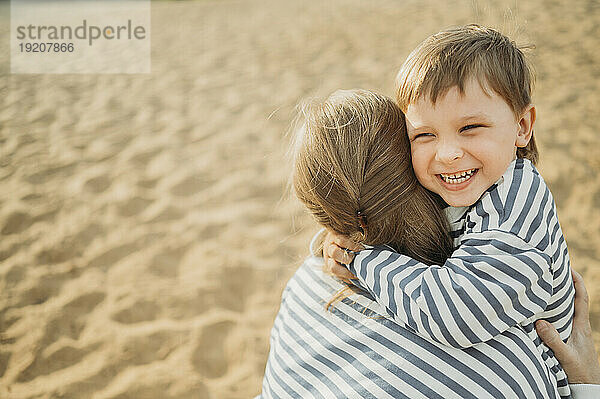 Mutter umarmt glücklichen Sohn am Strand