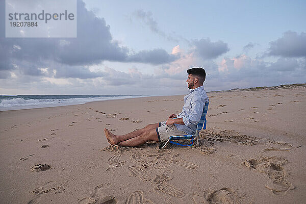 Man spending leisure time sitting on chair at beach