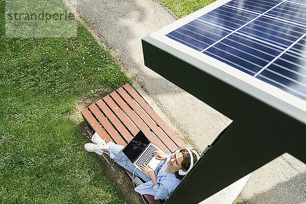 Lächelnde Frau sitzt unter einer Solarladestation im Park