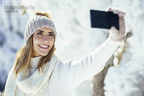 Glückliche Frau mit Mütze macht ein Selfie im Winterschnee