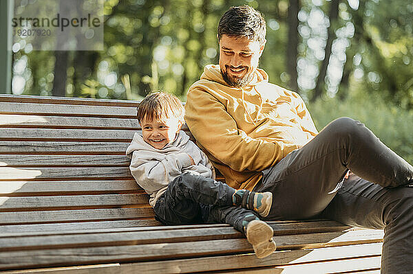 Lächelnder Vater und Sohn sitzen auf einer Bank im Park