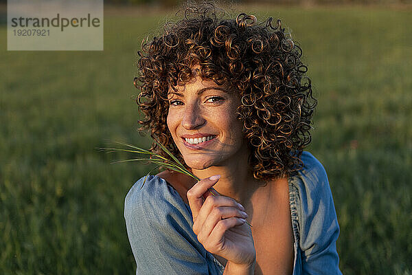 Happy woman with curly hair holding grass