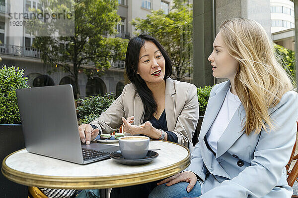 Geschäftspartner diskutieren mit Laptop und Kaffee am Tisch im Straßencafé