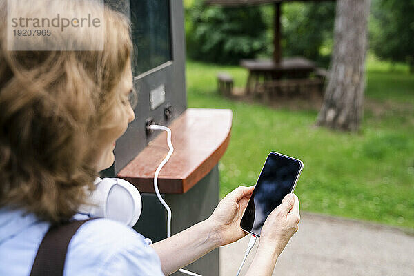 Frau hält Smartphone im Park  das durch Solarenergie aufgeladen wird