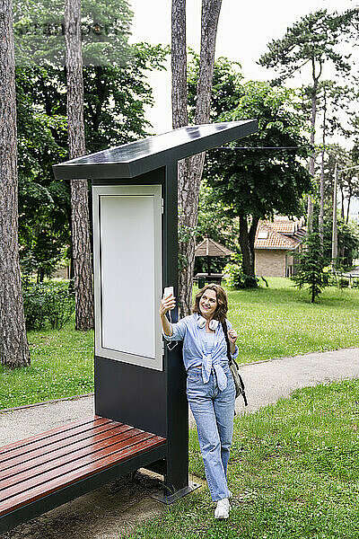 Frau macht Selfie mit Smartphone in der Nähe von Solarladestation im Park