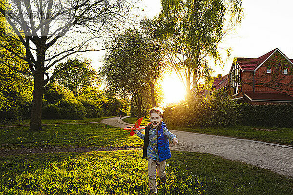 Fröhlicher Junge läuft bei Sonnenuntergang mit Spielzeugflugzeug