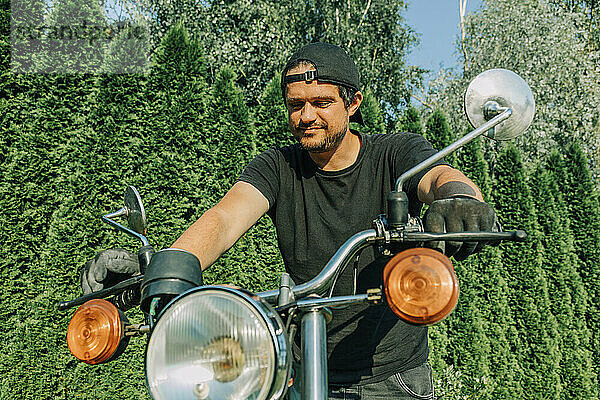 Lächelnder Mann untersucht Retro-Motorrad im Garten