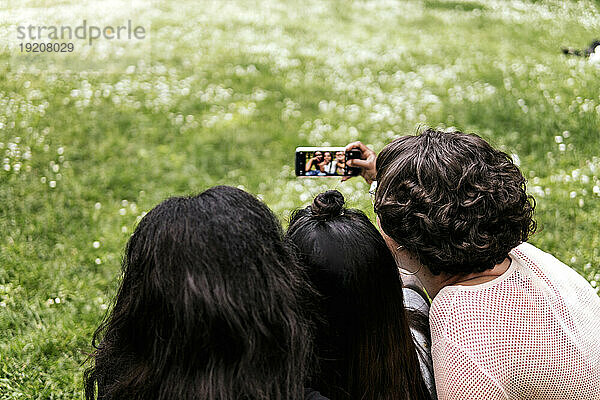 Woman taking selfie through smart phone with friends at park