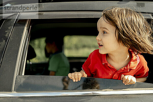 Boy with long hair leaning out of car window