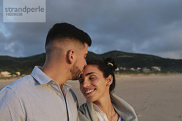 Young man kissing girlfriend at beach