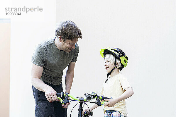 Glücklicher Vater und Sohn stehen mit dem Fahrrad vor der Wand