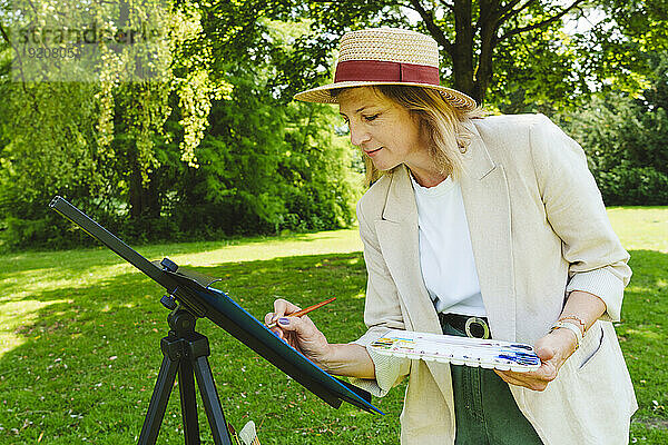 Reife Frau mit Hut malt im Park