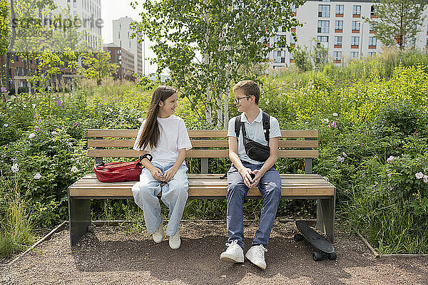 Smiling friends sitting on bench at park