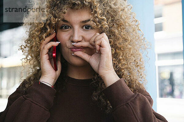 Junge Frau mit lockigem Haar telefoniert im Café
