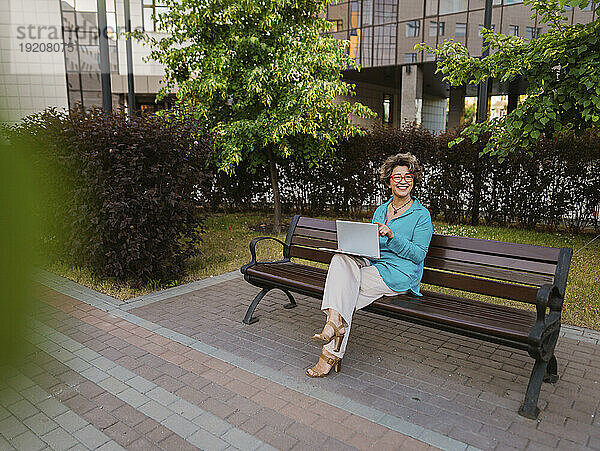 Glückliche Geschäftsfrau sitzt mit Laptop im Büropark