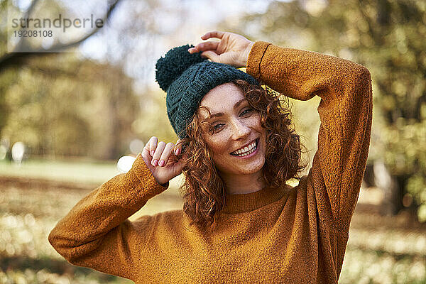 Cheerful redhead woman wearing knit hat at autumn park