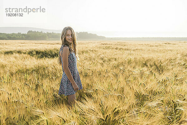 Lächelndes Mädchen  das inmitten der Ernte im Weizenfeld steht